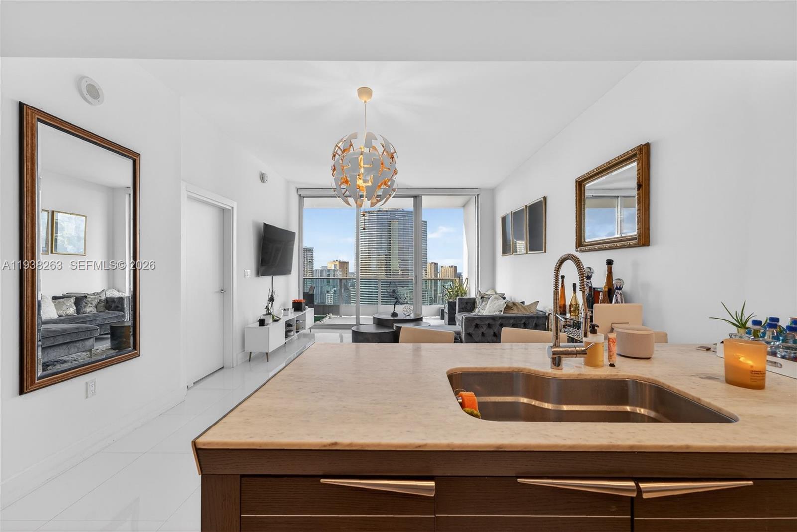 A modern kitchen island with a sink overlooks a living area with floor-to-ceiling windows — 200 Biscayne Boulevard Way # 4414, Miami FL 33131, MIAMI, FL