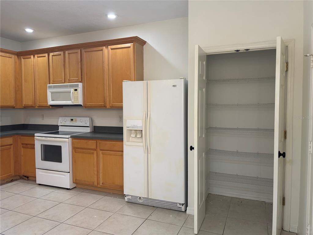 A kitchen featuring wood cabinets, white appliances, a pantry, and tile flooring — 3429 PARKRIDGE CIRCLE UNIT 19-103, SARASOTA, FL