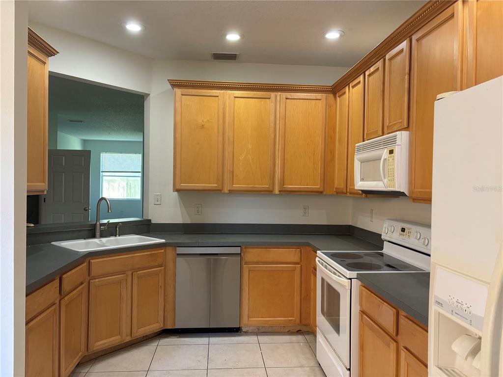 A kitchen features light wood cabinets, dark countertops, stainless steel appliances, and tile flooring — 3429 PARKRIDGE CIRCLE UNIT 19-103, SARASOTA, FL