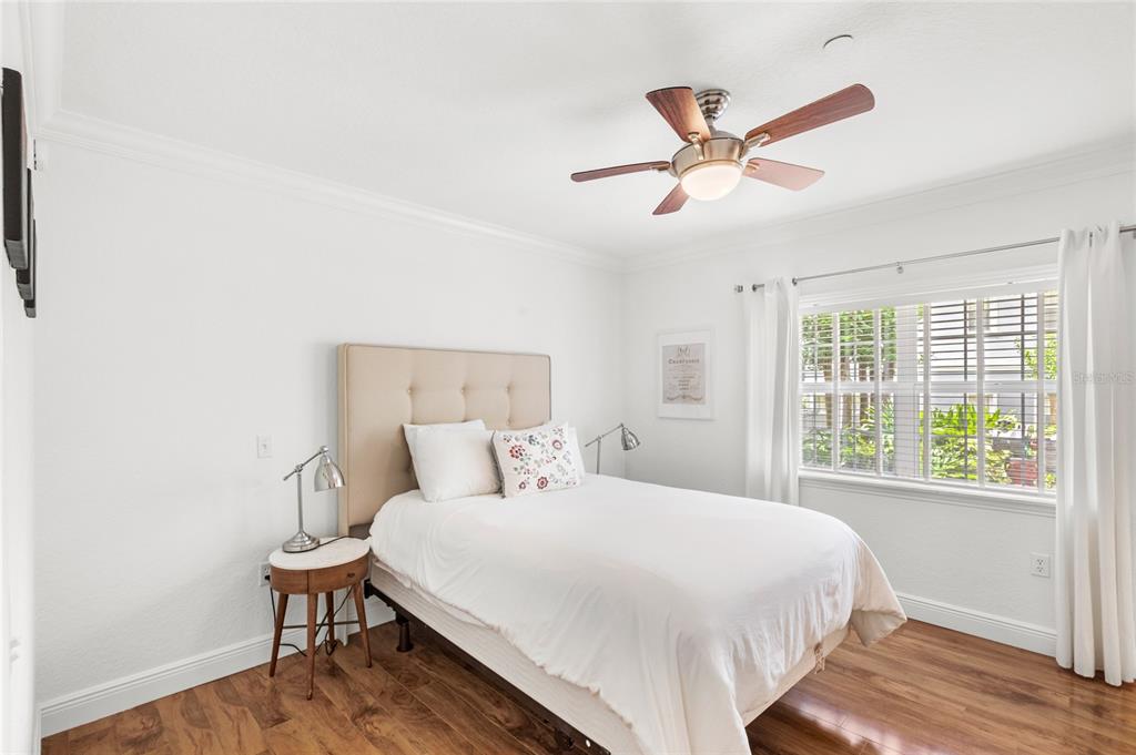 A bedroom features a bed with a beige headboard, wood flooring, and a ceiling fan — 7650 WHISPER WAY UNIT 104, REUNION, FL