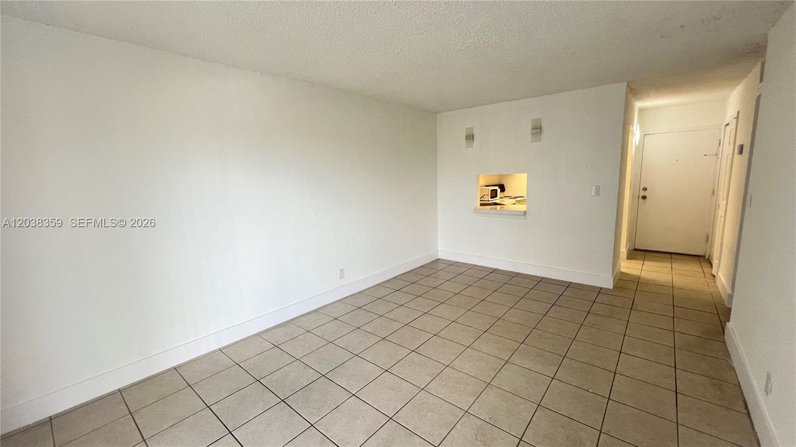 An empty room features beige tile flooring, white walls, and a small kitchen pass-through window — 4550 NW 9th St # 612E, Miami FL 33126, MIAMI, FL