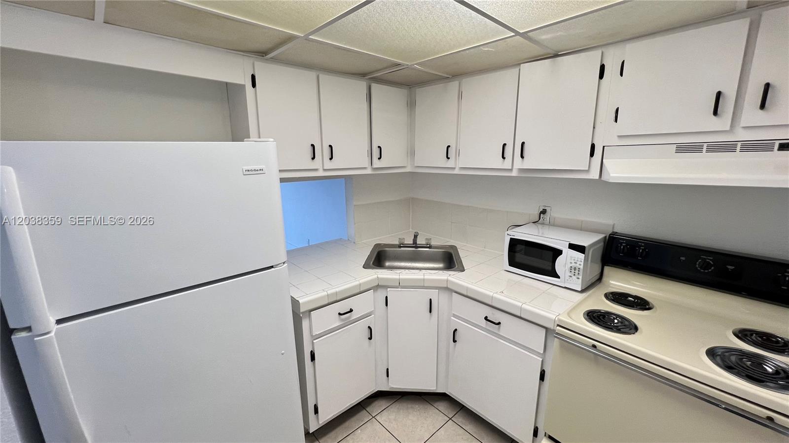A kitchen features white cabinets, tiled countertops, a corner sink, and white appliances — 4550 NW 9th St # 612E, Miami FL 33126, MIAMI, FL