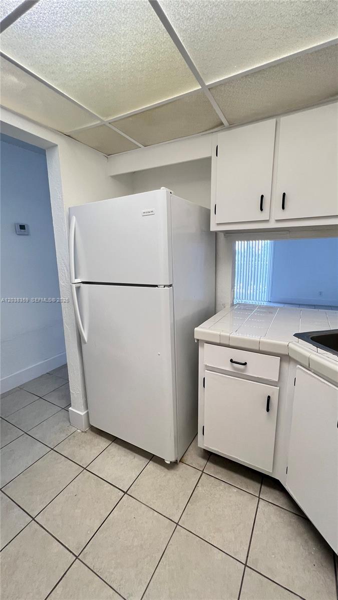 A kitchen features a white refrigerator, white cabinets, and light-colored tiled flooring — 4550 NW 9th St # 612E, Miami FL 33126, MIAMI, FL