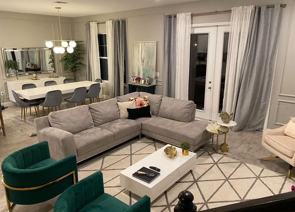 A living room with a gray sectional, green velvet chairs, and an adjacent dining area — 14739 GLADE HILL PARK WAY, WINTER GARDEN, FL