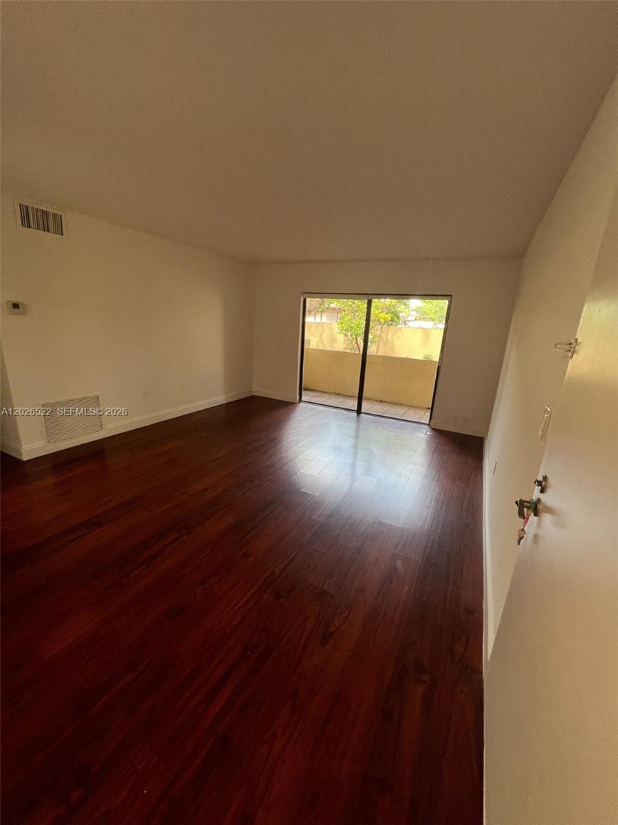 An empty room features dark wood flooring, white walls, and a sliding glass door — 10415 N Kendall Dr # B113, Miami FL 33176, MIAMI, FL