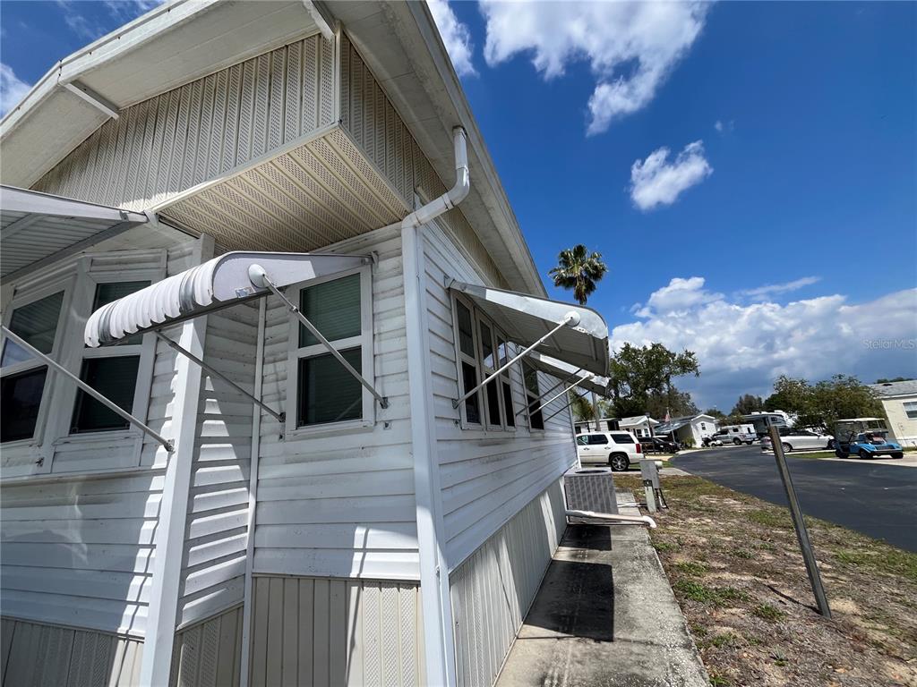 The exterior of a white mobile home features metal window awnings and vertical siding — 7392 INTERNATIONAL CIRCLE, LAKE WALES, FL