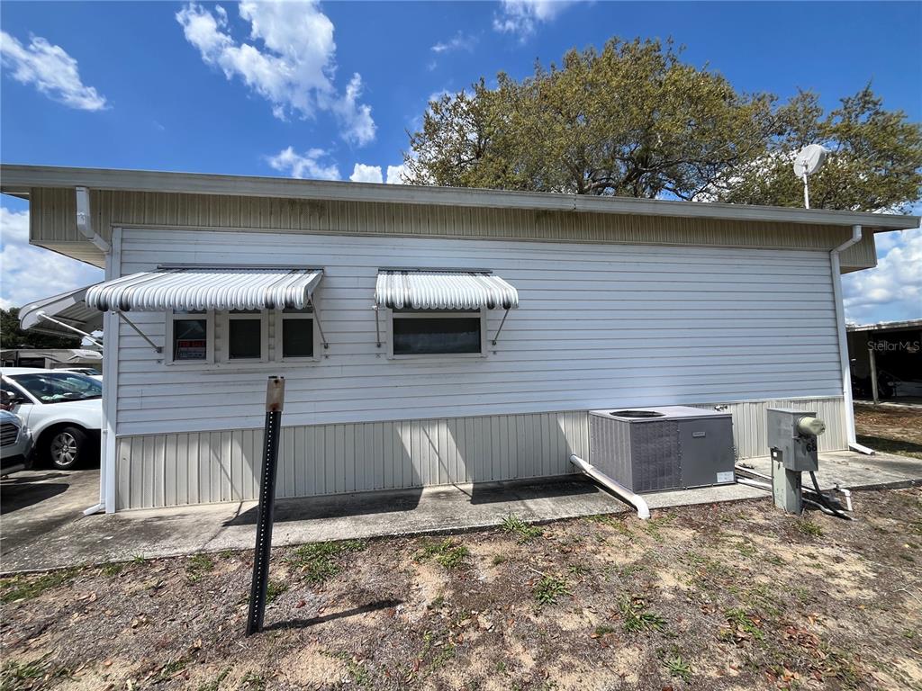 The exterior side of a white mobile home features metal awnings and an HVAC unit — 7392 INTERNATIONAL CIRCLE, LAKE WALES, FL