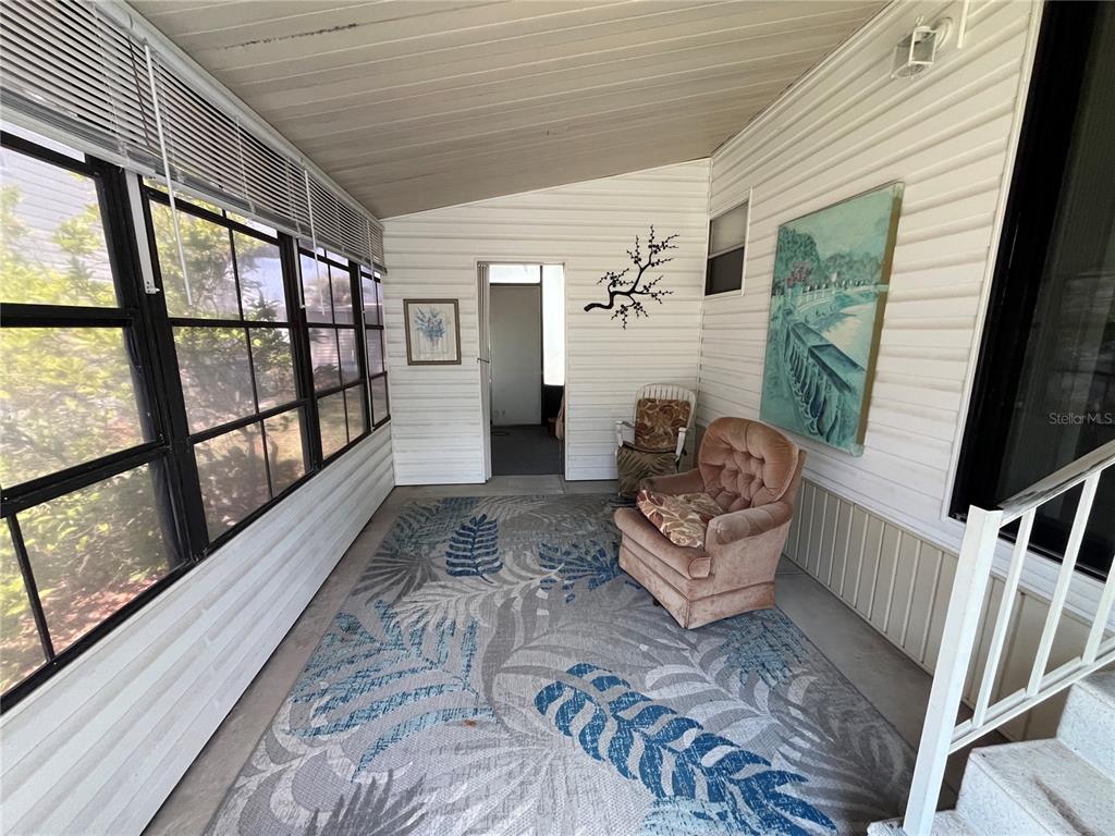 A sunroom features a large patterned rug, two armchairs, wall art, and windows with blinds — 7392 INTERNATIONAL CIRCLE, LAKE WALES, FL