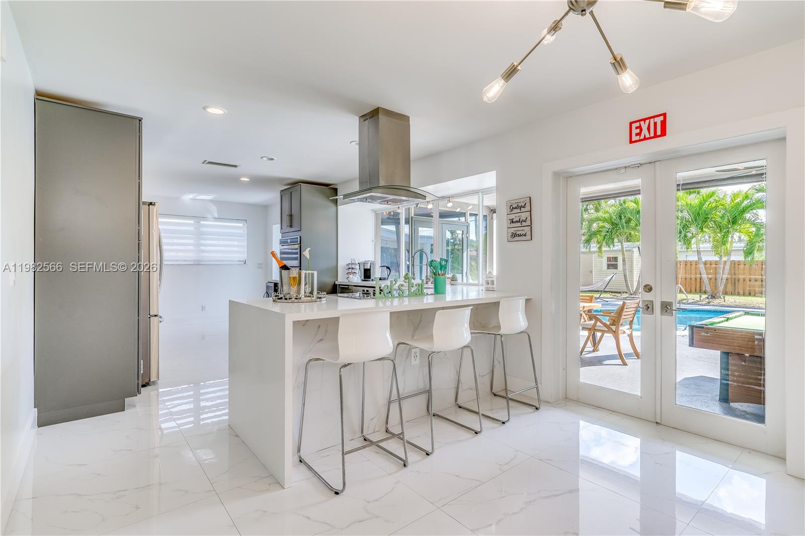 A modern kitchen features a marble-topped island with bar stools and an exit door — 4212 Van Buren St, Hollywood FL 33021, HOLLYWOOD, FL