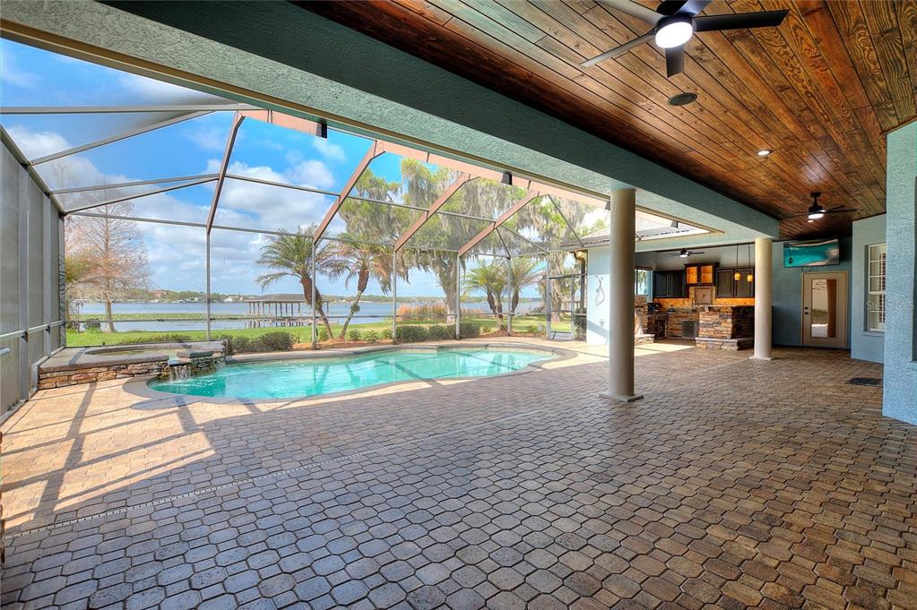 A covered patio features a pool, spa, and outdoor kitchen overlooking a lake — 4848 ISLAND SHORES LANE, LAKELAND, FL