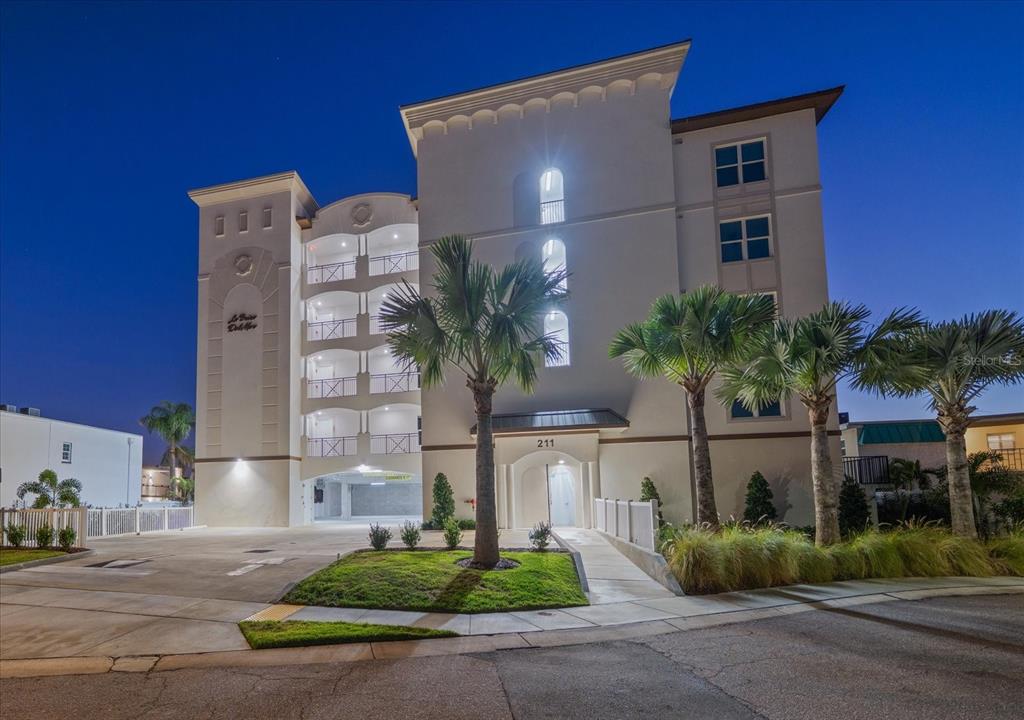 A multi-story residential building with balconies, palm trees, and a ground-level parking area at dusk — 211 DOLPHIN POINT UNIT 203, CLEARWATER, FL