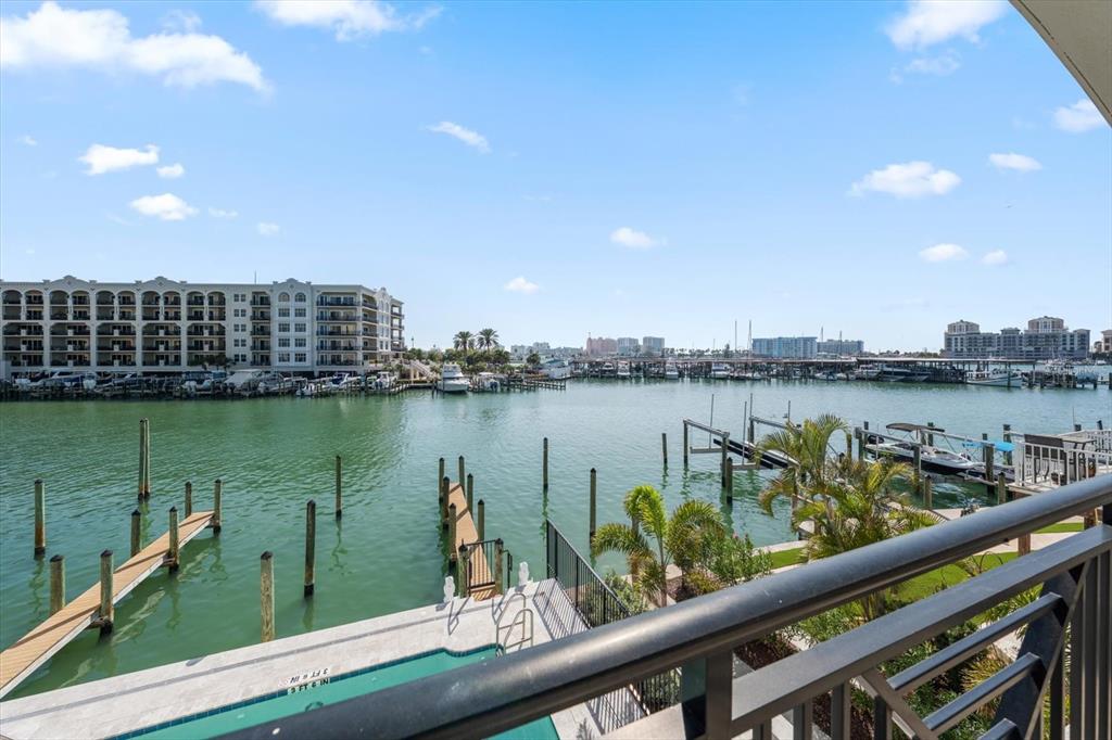 A balcony view overlooking a marina with boats, docks, a swimming pool, and apartment buildings — 211 DOLPHIN POINT UNIT 203, CLEARWATER, FL