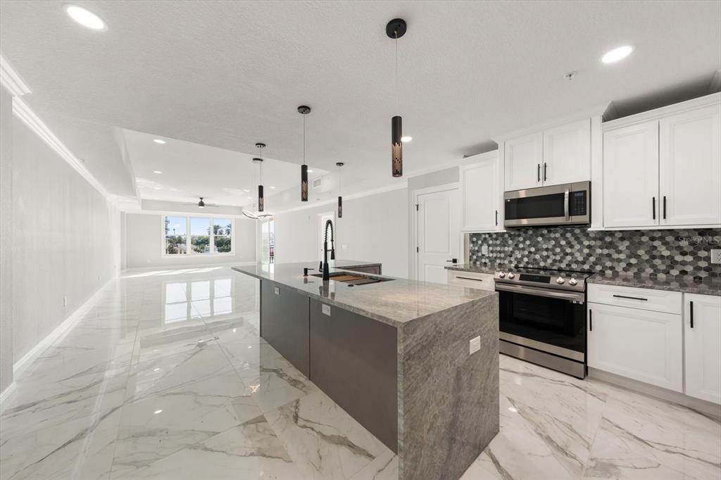 A modern kitchen with white cabinets, a gray stone island, and white marble-look tile flooring — 211 DOLPHIN POINT UNIT 203, CLEARWATER, FL