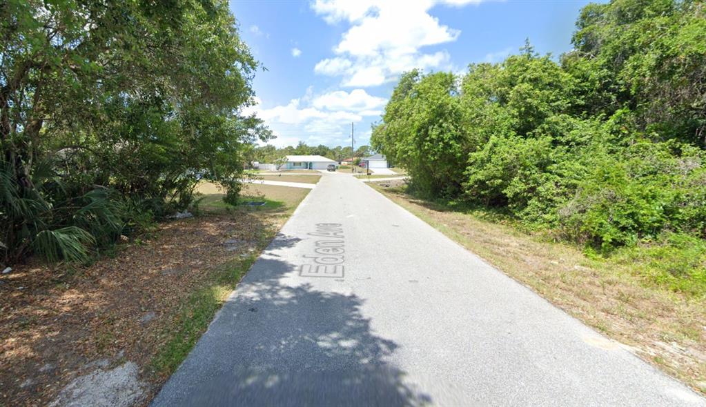 A paved residential street lined with dense trees leads toward houses in the distance — 1272 EDEN AVENUE, PORT CHARLOTTE, FL