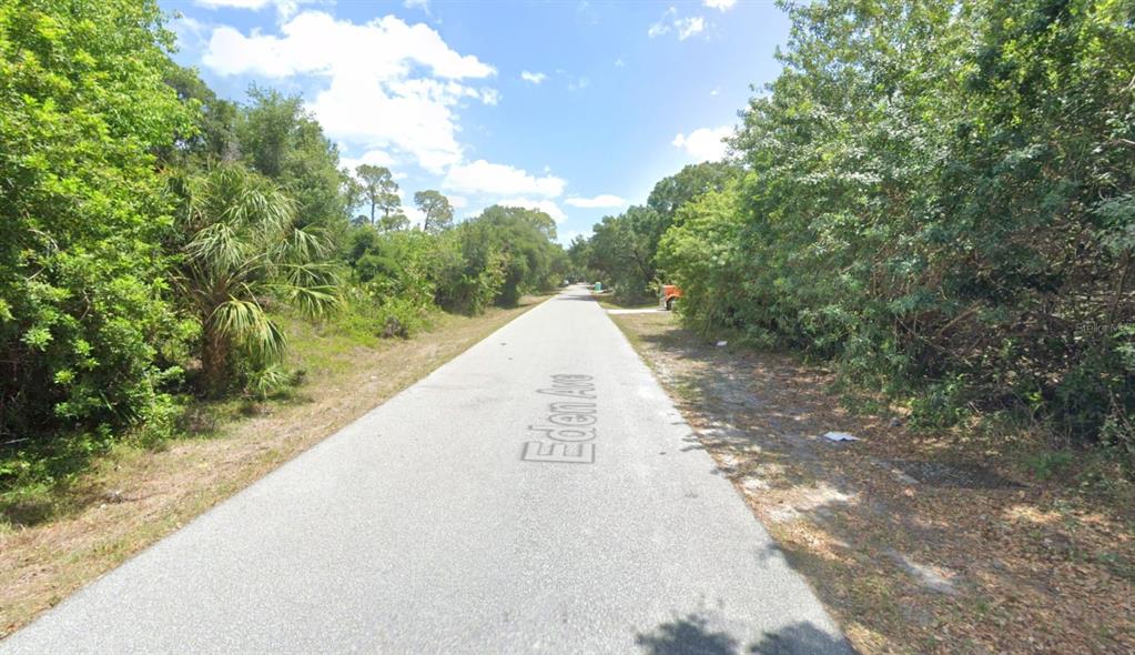 A paved road stretches into the distance, flanked by dense trees and lush vegetation — 1272 EDEN AVENUE, PORT CHARLOTTE, FL
