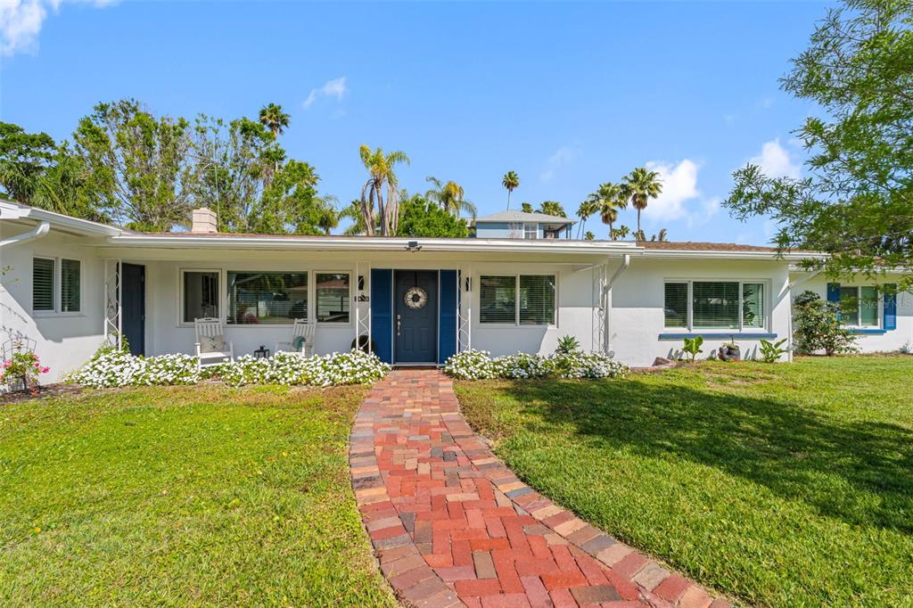 A white single-story house features a brick walkway leading to a blue front door — 1794 SANTA BARBARA DRIVE, DUNEDIN, FL