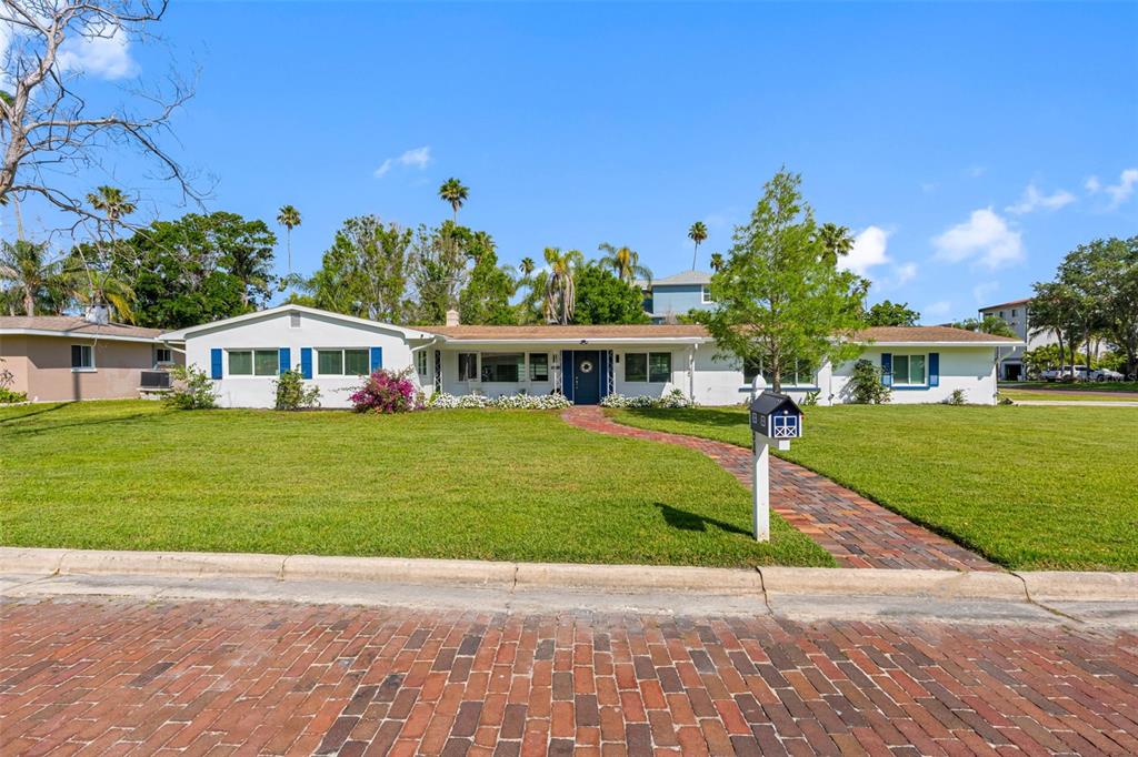 A single-story white house with blue shutters sits behind a brick walkway and lawn — 1794 SANTA BARBARA DRIVE, DUNEDIN, FL