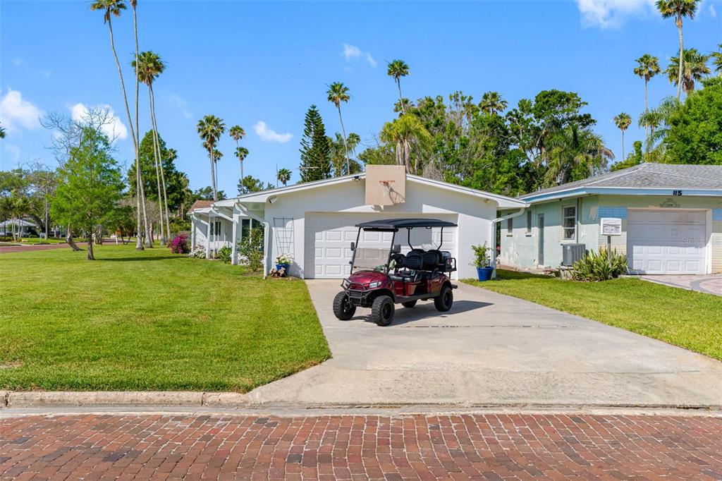 A golf cart is parked on the concrete driveway in front of a white house — 1794 SANTA BARBARA DRIVE, DUNEDIN, FL