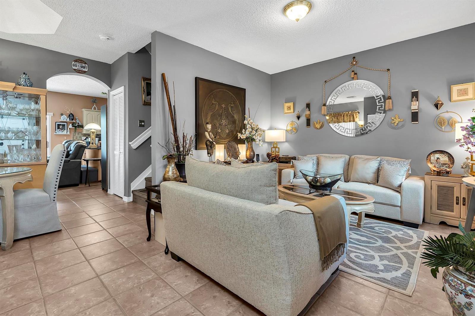 A living room with gray walls, tile flooring, a beige sofa, and a round wall mirror — 16637 NW 73rd Place, Miami Lakes FL 33014, MIAMI LAKES, FL