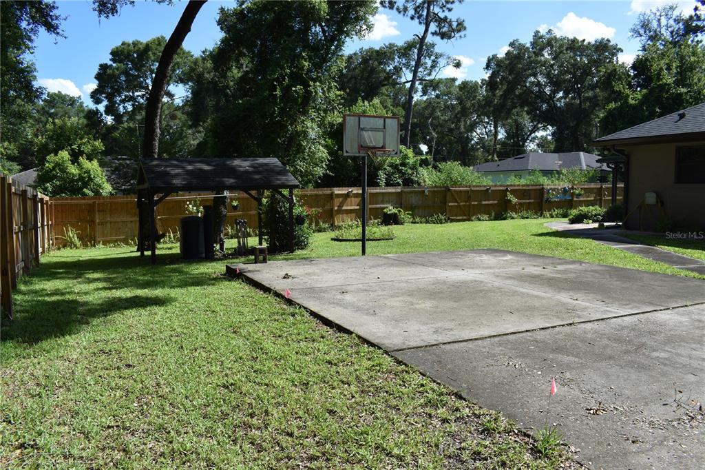 A backyard features a concrete basketball court, a wooden gazebo, and a wooden privacy fence — 1250 15TH STREET, ORANGE CITY, FL