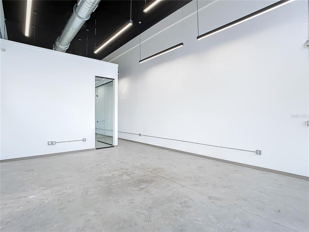 An empty commercial space features concrete floors, white walls, exposed ductwork, and modern linear lighting — 12324 W COLONIAL DRIVE, WINTER GARDEN, FL
