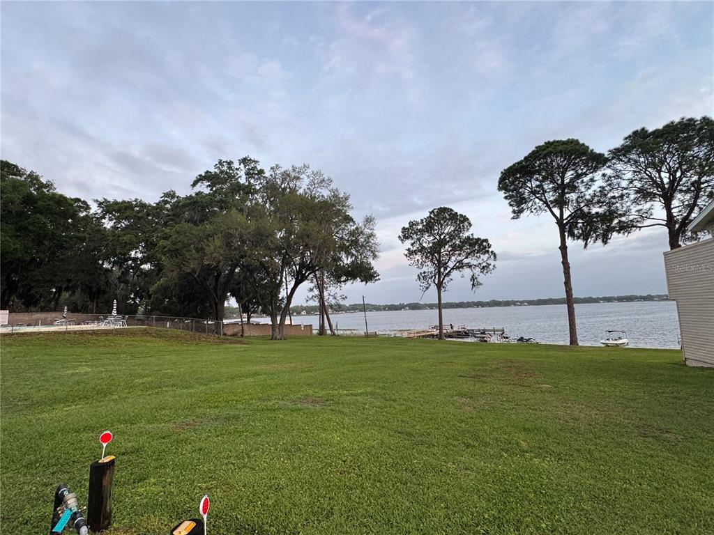 A large grassy yard leads to a lake with trees and a small boat dock — 11001 SE SUNSET HARBOR ROAD UNIT D21, SUMMERFIELD, FL