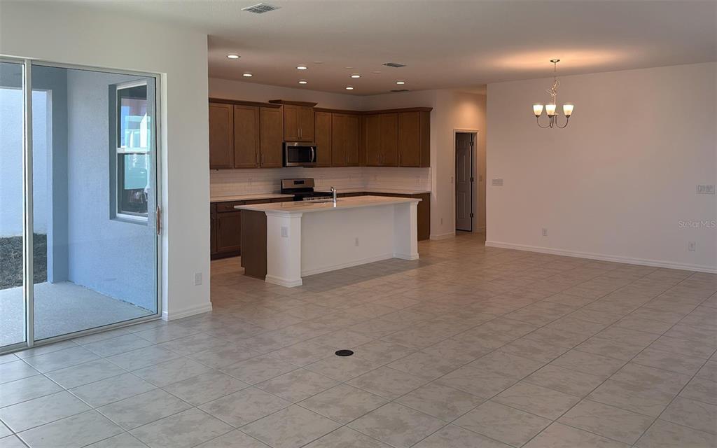 An open-concept kitchen features wood cabinets, a white island, and tile flooring — 6863 SPANISH IMPERIAL STREET, HOWEY IN THE HILLS, FL