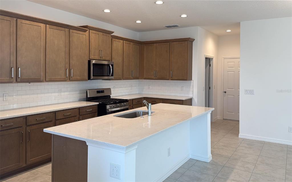 A kitchen with wood cabinets, white countertops, a center island, and a white tile backsplash — 6863 SPANISH IMPERIAL STREET, HOWEY IN THE HILLS, FL