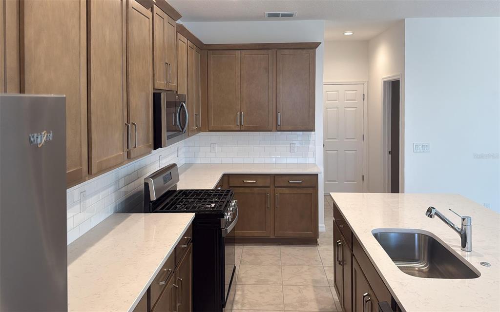 A kitchen features brown cabinets, white countertops, a subway tile backsplash, and a center island — 6863 SPANISH IMPERIAL STREET, HOWEY IN THE HILLS, FL