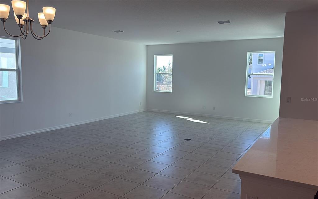 A spacious, empty room features light-colored tile flooring, white walls, and a modern chandelier — 6863 SPANISH IMPERIAL STREET, HOWEY IN THE HILLS, FL