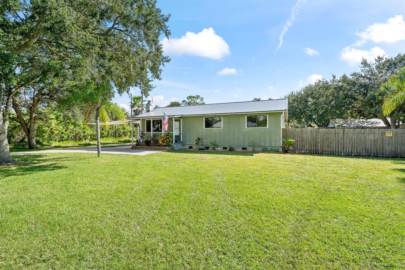 A single-story green house with a metal roof sits on a large grassy lot — 9633 Honeysuckle, FL 32976, FL