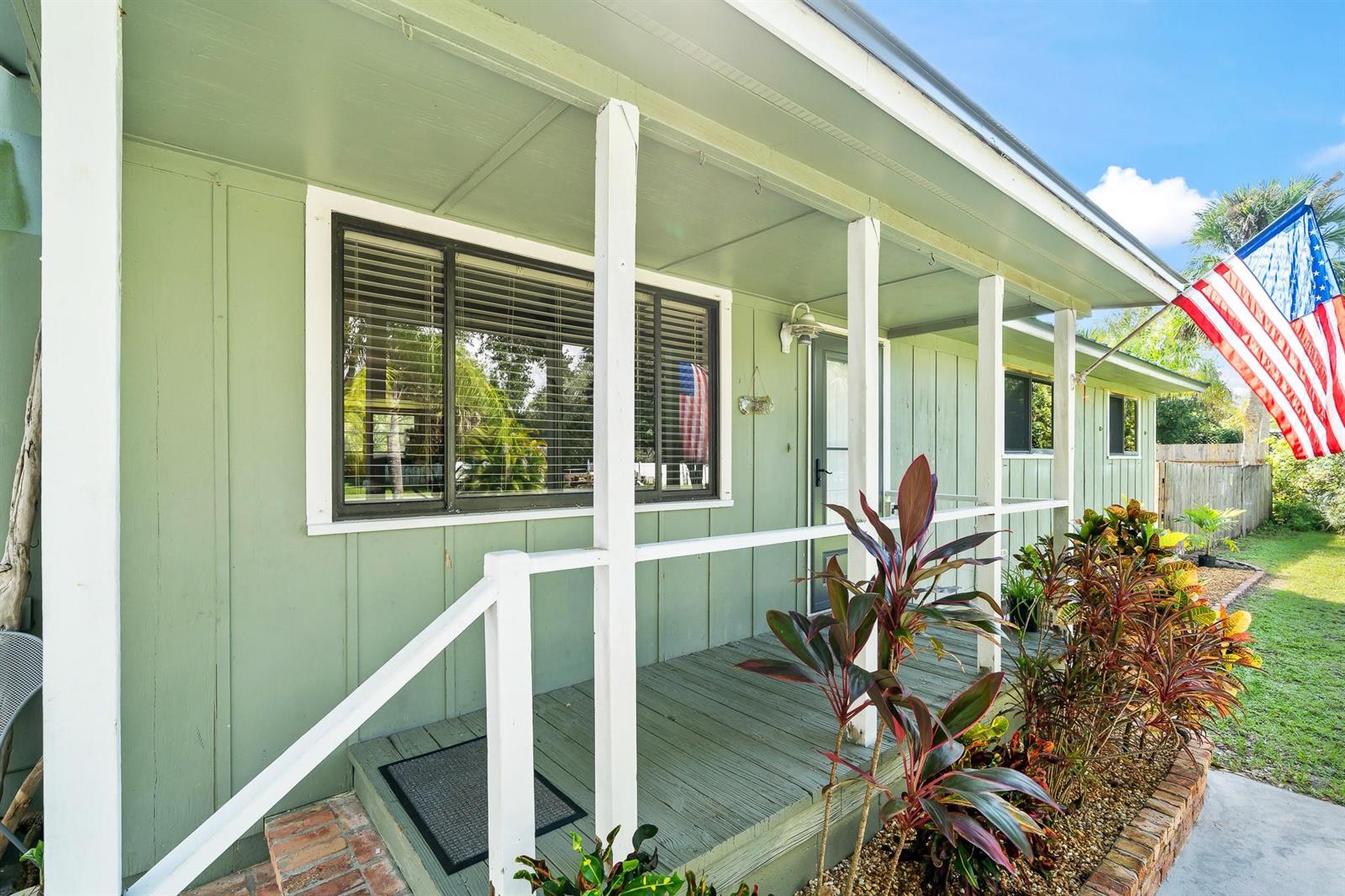 A light green house exterior features a covered porch with white railings and a flag — 9633 Honeysuckle, FL 32976, FL