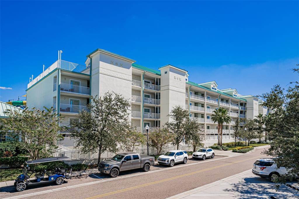 A multi-story white apartment building with balconies stands beside a road with parked cars — 399 2ND STREET UNIT 215, INDIAN ROCKS BEACH, FL