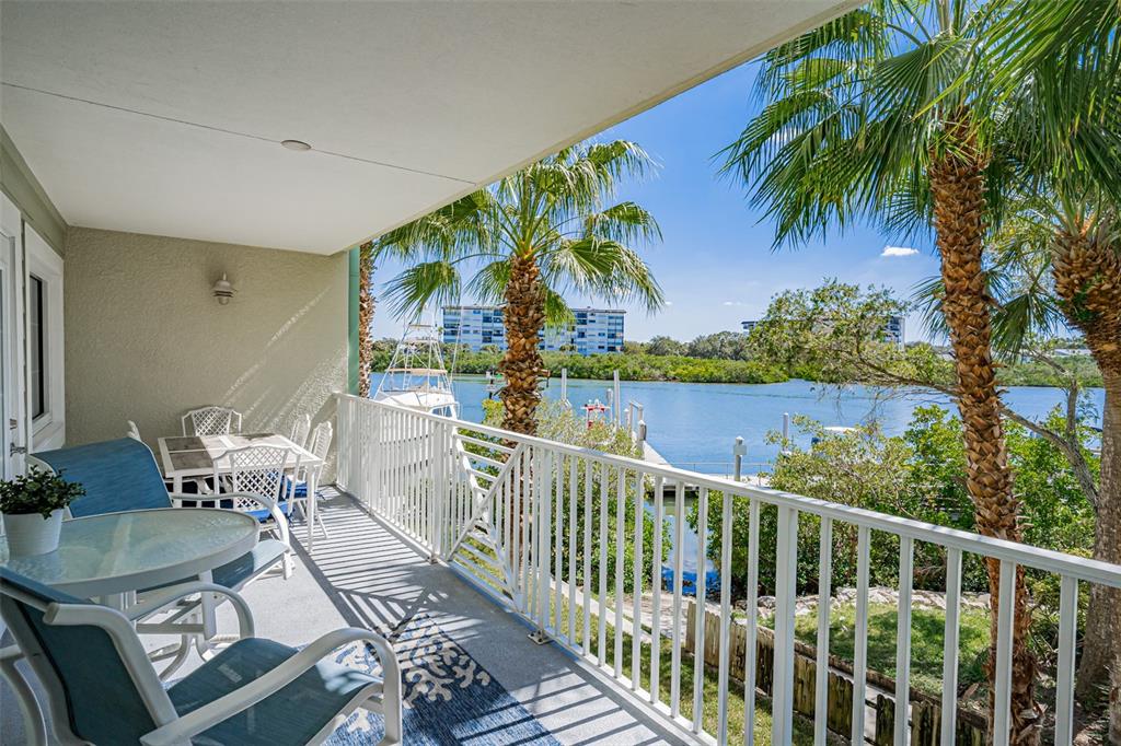 A covered balcony with outdoor furniture overlooks a marina, palm trees, and a waterway — 399 2ND STREET UNIT 215, INDIAN ROCKS BEACH, FL