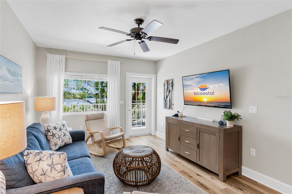 A living room features a blue sofa, a wicker coffee table, and a wall-mounted television — 399 2ND STREET UNIT 215, INDIAN ROCKS BEACH, FL