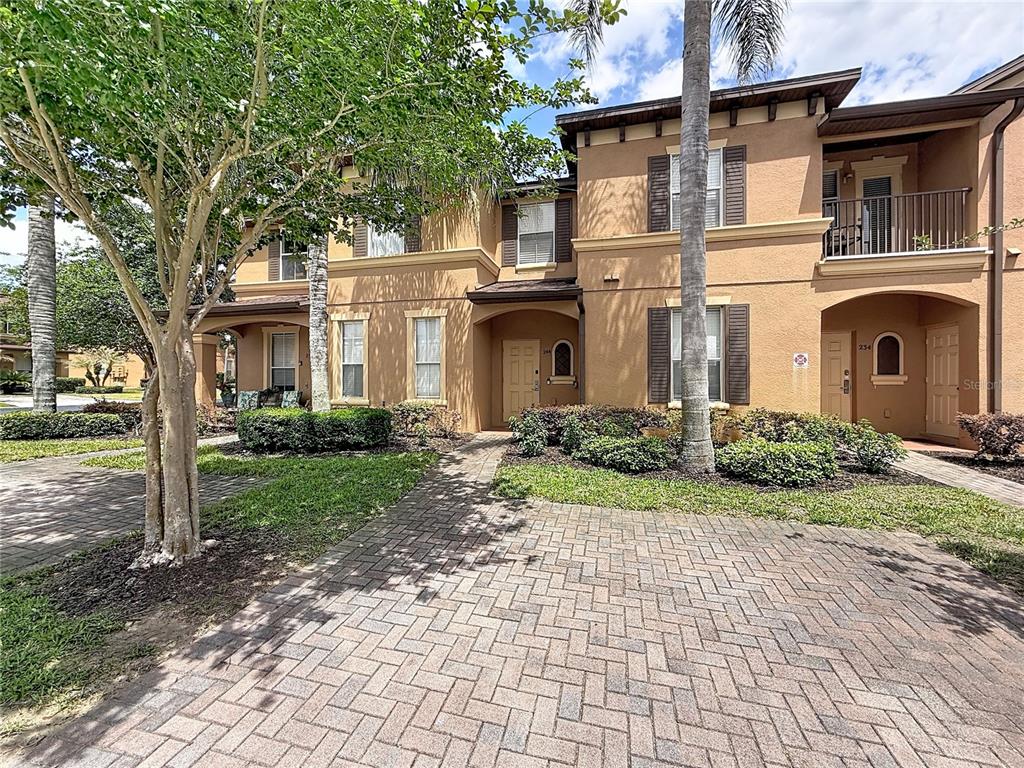 A two-story tan stucco townhouse with a brick paver driveway and a second-floor balcony — 244 CAPRI DRIVE, DAVENPORT, FL