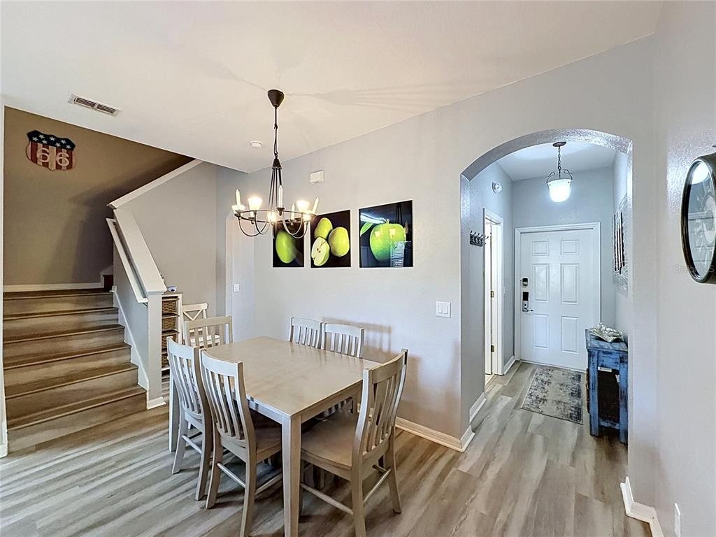 A dining area with a wooden table and chairs sits beside a staircase and entryway — 244 CAPRI DRIVE, DAVENPORT, FL