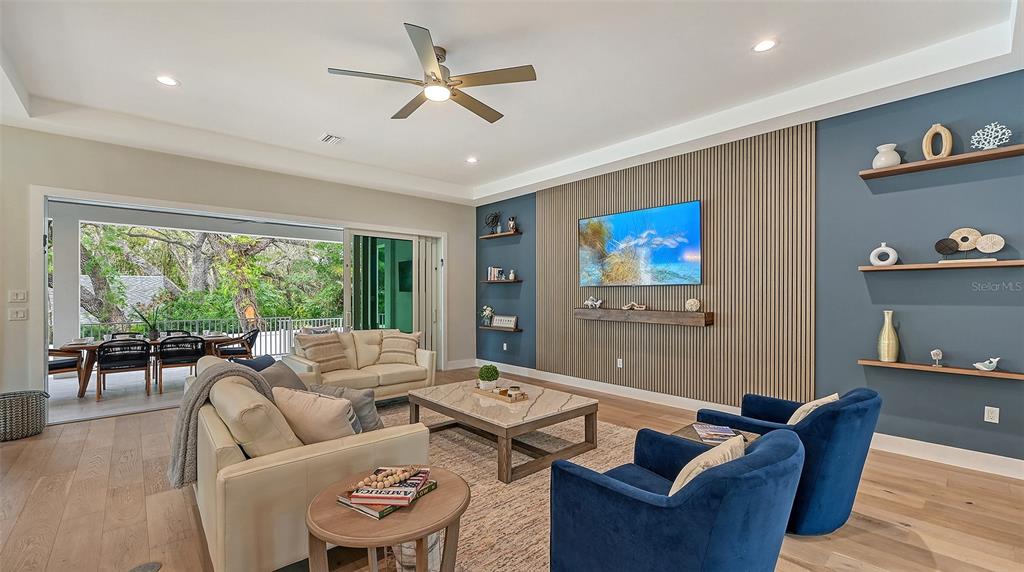 A living room features a slatted wood accent wall, blue shelving, and sliding glass doors — 1537 SIESTA DRIVE, SARASOTA, FL