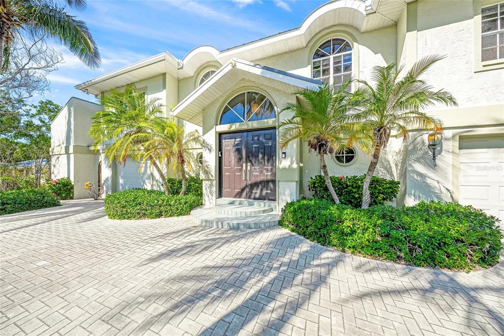 The exterior of a two-story house features a paved driveway, double front doors, and palm trees — 569 JUAN ANASCO DRIVE, LONGBOAT KEY, FL