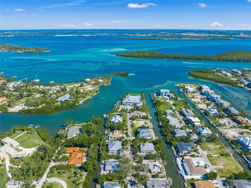 An aerial view shows a coastal neighborhood with a white-circled house near a canal — 569 JUAN ANASCO DRIVE, LONGBOAT KEY, FL