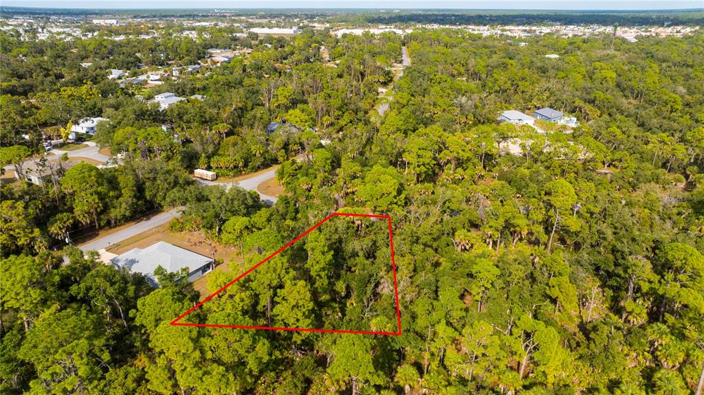 An aerial view shows a wooded, triangular-shaped plot of land outlined in red — 14091 SLICHTER AVENUE, PORT CHARLOTTE, FL