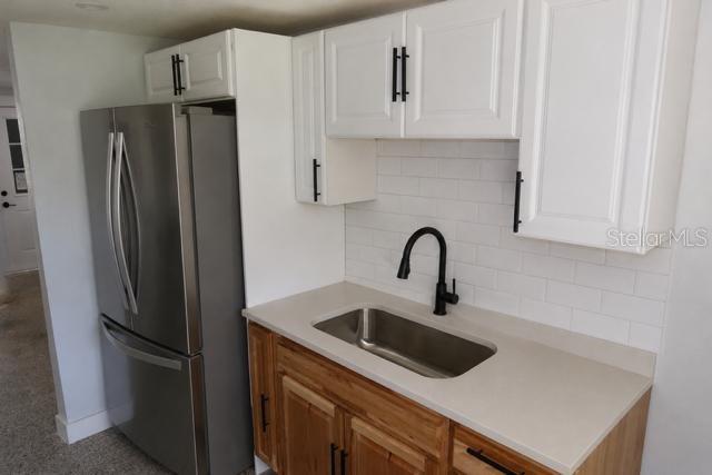 A kitchen area features a stainless steel refrigerator, wood cabinets, white upper cabinets, and sink — 559 NASTURTIUM AVENUE, SEBRING, FL
