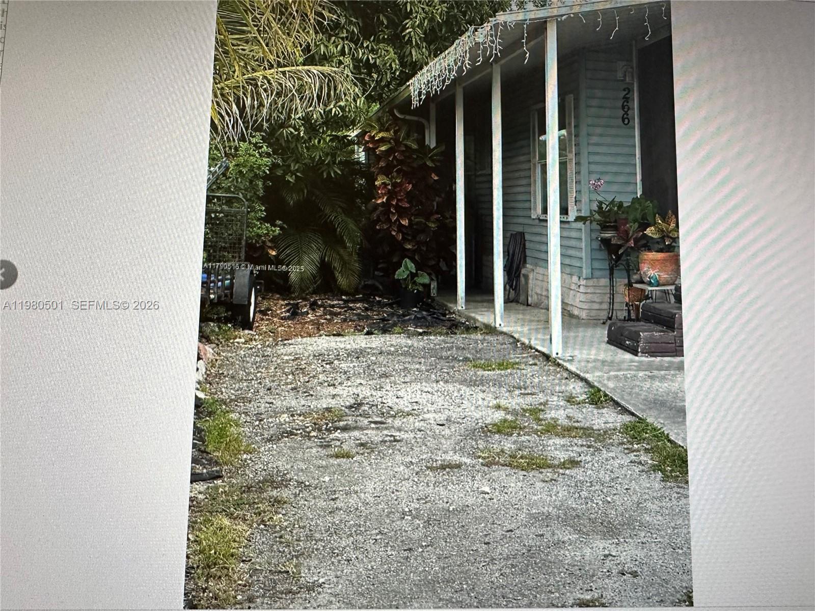 A gravel driveway leads to the covered porch of a light blue single-story house — 19800 SW 180th Ave Lot 266, Miami FL 33187, MIAMI, FL