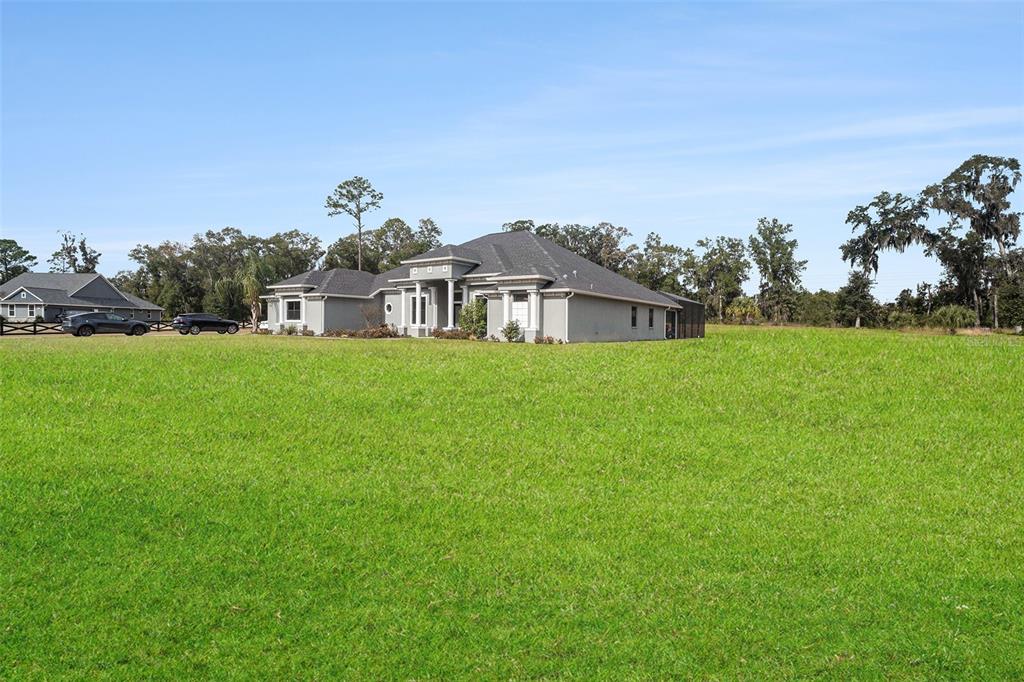 A grey single-story house sits on a large, open green lawn under a clear sky — 7403 NE 22ND COURT ROAD, OCALA, FL