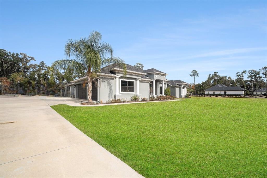 A single-story gray house with a palm tree and a large concrete driveway — 7403 NE 22ND COURT ROAD, OCALA, FL
