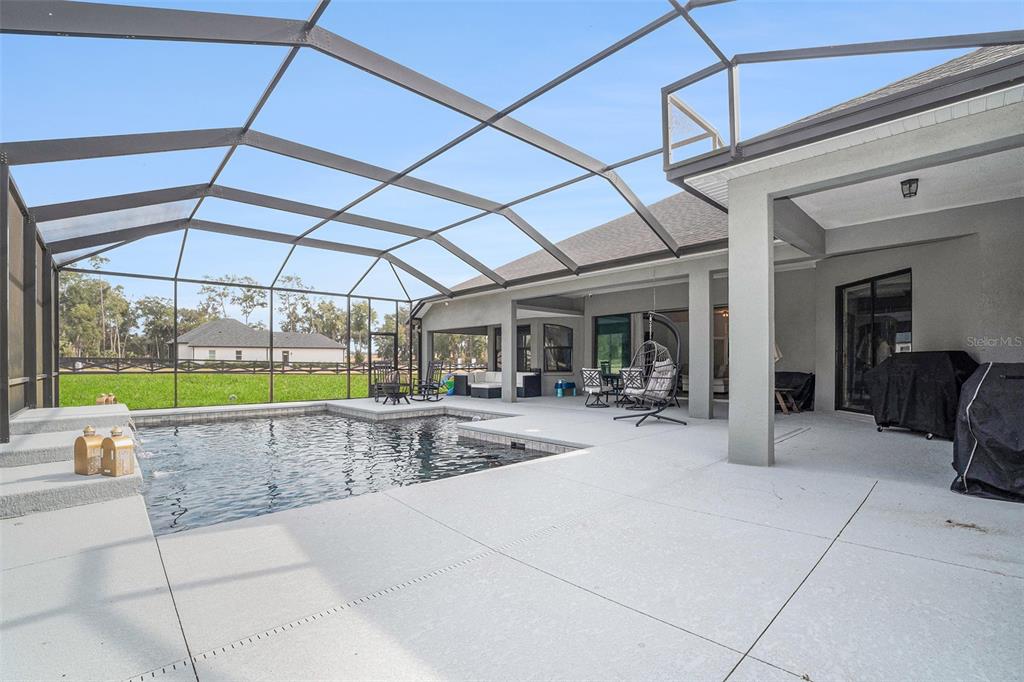 A screened-in patio features a swimming pool, concrete decking, and a covered seating area — 7403 NE 22ND COURT ROAD, OCALA, FL
