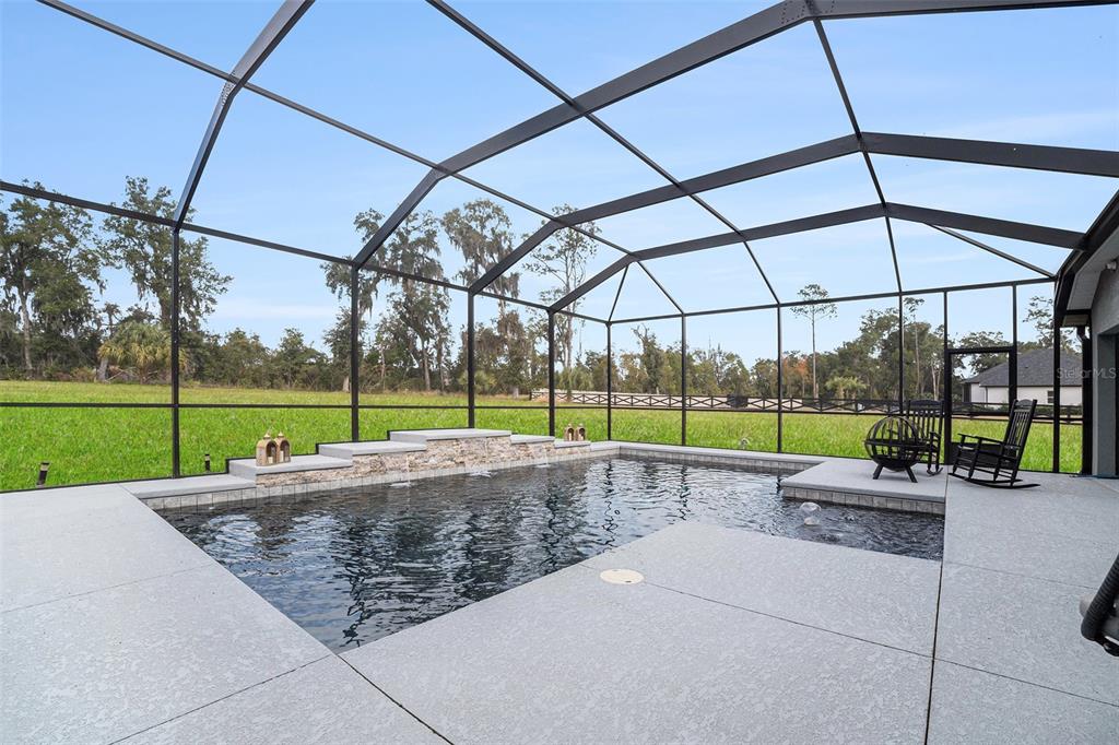 A screened-in swimming pool with a stone water feature and a concrete deck — 7403 NE 22ND COURT ROAD, OCALA, FL