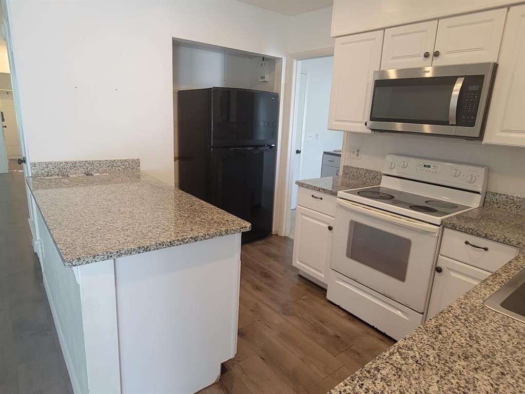 A kitchen features white cabinets, granite countertops, a black refrigerator, and a stainless steel microwave — 6290 CONISTON TERRACE, NORTH PORT, FL