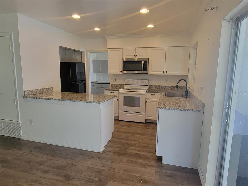 A kitchen with white cabinets, granite countertops, stainless steel appliances, and wood-look flooring — 6290 CONISTON TERRACE, NORTH PORT, FL