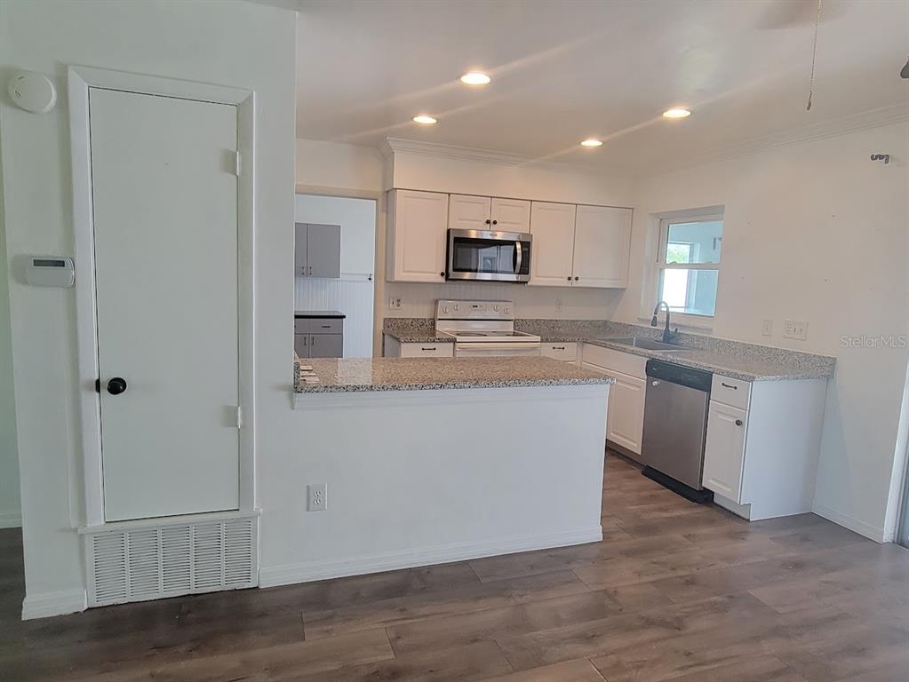 A kitchen with white cabinets, granite countertops, stainless steel appliances, and wood-look flooring — 6290 CONISTON TERRACE, NORTH PORT, FL